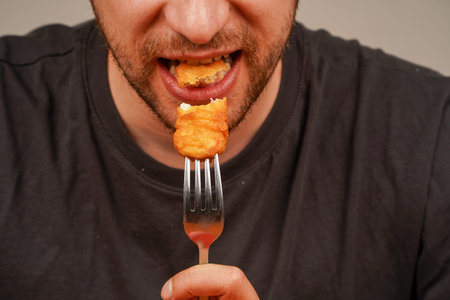 A close-up of a man eating a golden crispy nuggets highlights the moment of fast food enjoyment. A...