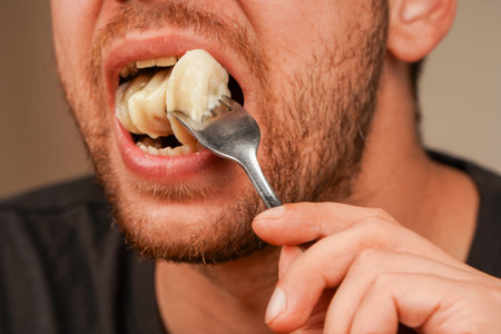 A detailed shot of a dumpling on a fork near an open mouth, focusing on the textures of the food and...