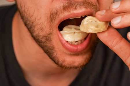A man puts a vareniki into his mouth, demonstrating the joy of delicious home cooking. A man eats pelmeni with his hands.の写真素材