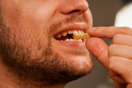 A man prepares to enjoy a crunchy treat, delicately holding it near his open mouth. The emphasis on the dry bread snack adds to the sense of appetite.の写真素材