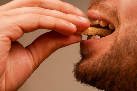 Close-up of a man eating a crispy bread snack while holding it in his hand. The natural expression and detailed texture of the rusk create a dynamic and appetizing moment.の写真素材