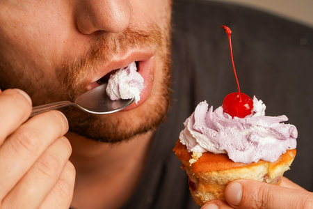 Close-up of a man enjoying a piece of cake with a cherry and cream frosting with a spoon. As a concept, life in pleasure, dessert and the desire for something sweet.の写真素材