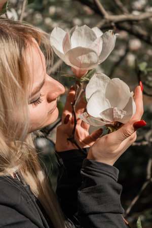 A close-up of a blonde girl posing for a photo in front of a blooming magnolia. Spring flowers emphasize the beauty of the moment and the young woman.の写真素材