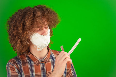 The curly-haired boy gently rubs foam across his face, the vibrant green chroma key enhancing the clean and dynamic nature of the visual.の写真素材