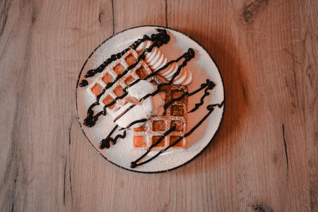 Waffle on wooden table. Top view. Served with ice cream. Belgian waffles with banana, ice cream and chocolate on top. Sweet dessert waffles. Delicious dessert for tea time.の写真素材