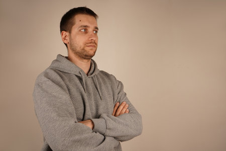 Man looking at camera. Crossed hands. Side view. Neutral background. Male in casual clothes. Young guy standing in front of camera.の写真素材