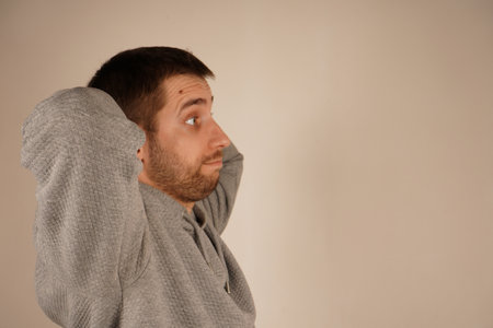 Crossed hands over head. Young guy standing in front of camera with neutral background. Male looking at camera front view. Man in casual clothes.の写真素材