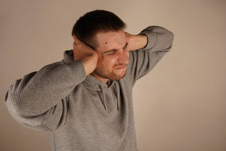 Photo of bearded man keeps hands on head and closes eyes. Portrait of young guy closing his ears by...