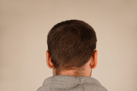 A close-up of a mans head with dark hair, viewed from behind. The texture of his hair is clear, and...