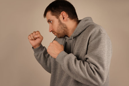 Wearing a sports hoodie, the man stands with fists clenched, prepared for action. His pose resembles...
