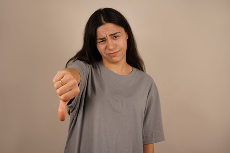 The scene evokes a strong negative reaction. The woman holds her hand with her thumbs down, clearly expressing displeasure. Her serious expression reinforces the message of dislike.の写真素材