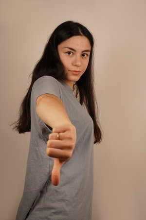 The woman holds her hand with her thumbs down, clearly expressing displeasure. Her serious expression reinforces the message of dislike. The scene evokes a strong negative reaction.の写真素材