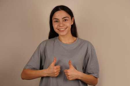 With both hands showing a thumbs up, the woman expresses strong approval. Her enthusiastic posture...