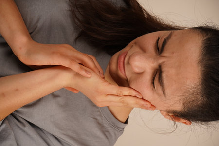 A young woman holds her gum with one hand, her expression showing discomfort. The gesture clearly reflects toothache or pain. The scene conveys a relatable moment of physical unease.の写真素材