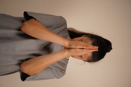 The woman holds her hands by her head. A young woman with dark hair clasps her hands, her palms pressed together. Her calm expression conveys sincere devotion and a moment of reflection.の写真素材