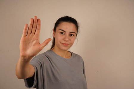 A smiling girl waves her hand in a cheerful greeting, radiating warmth. Her casual demeanor creates...
