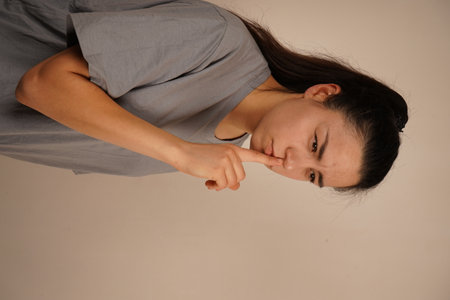 The facial expression is calm but firm, indicating a request for silence or secrecy. A subtle and timeless gesture, understood by all. One finger placed on the lips signals a gesture of silence.の写真素材