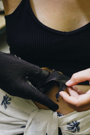 A woman in a glove shows off a bat indoors. A wonderful moment of wildlife and human interaction.