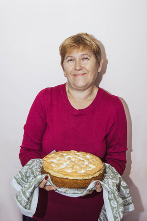 An elderly woman holds a freshly baked cake in her hands. Grandma is preparing a pie in the home kitchen. Homemade healthy food. The process of making pies with your own hands.の写真素材