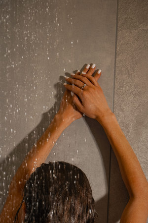 A girl with wet hair in the shower stands with her back to the water drops in a black nightgown with...