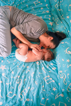 A beautiful mother lies on the bed next to a sleeping baby,strokの写真素材