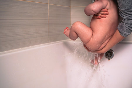 Bathing a newborn baby in a bathtub. Bathing your son in warm water. Happy adorable newborns smile in the bath relaxing and comfortable. The concept of caring for a newborn baby.の写真素材