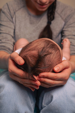 Mother with newborn baby boy hugging him tenderly holding him on her lap on white isolated...