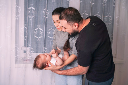 Happy young mother and father standing together in a room at home, cradling their newborn son.