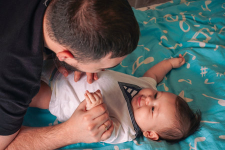 The baby in a white bodysuit looks up with curiosity, as the father leans closer to share this...