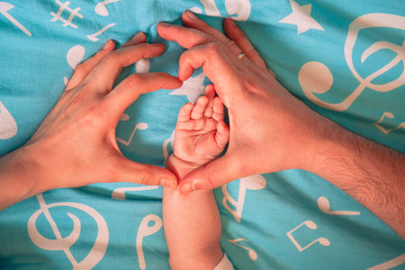The newborns tiny feet are embraced by heart-shaped hands, a powerful symbol of parental love and unity.の写真素材