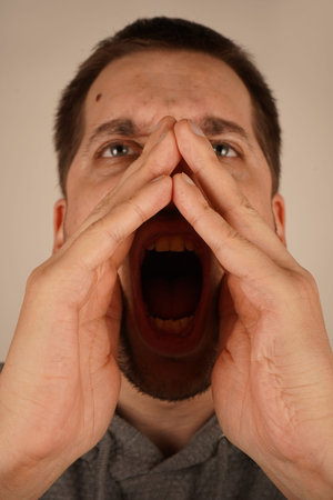 The scene captures his dramatic gesture. A young man with dark hair places his hands near his mouth,...