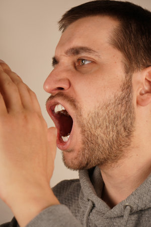 The image conveys excitement and energy. With dark hair and a lively expression, the man cups both hands over his mouth, resembling a megaphone. His actions suggest a loud announcement.の写真素材