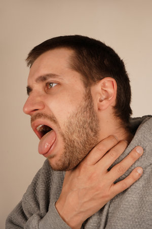 The discomfort on his face shows the urgency of the moment, as he struggles with breathing or a strong cough. A man grips his throat with his hand, mouth wide open as if he s choking or coughing.の写真素材