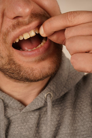 A young man carefully removes something from his teeth. His focused expression highlights the attention to detail in this delicate action. The image captures his precise movement.の写真素材