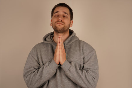 The young man, dressed in athletic wear, places his palms together in a prayer gesture. His expression is calm, creating a sense of earnest prayer or quiet reflection. It's a moment of connection.の写真素材