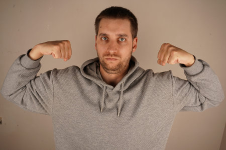 Flexing both arms, the man demonstrates his biceps and clenched fists. His pose emphasizes his...