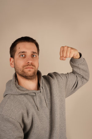 His pose reflects both physical strength and confidence. The smile makes the gesture feel friendly and motivating. With a cheerful smile, the young man flexes his arm, highlighting his strong bicep.の写真素材