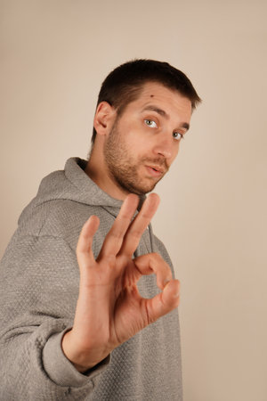 With a smile, the man forms the "OK" gesture using his hand. His expression is friendly and reassuring, conveying a sense of approval. Its a simple, positive gesture full of warmth.の写真素材