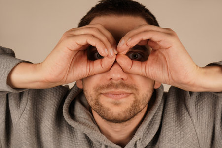 A man playfully makes a circle with his fingers around his eyes, imitating glasses. His gesture adds a fun and quirky element to his expression. This playful moment brings a sense of humor.の写真素材
