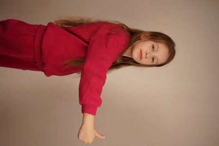 A girl with striking red hair raises her hand in a "thumbs up" gesture, expressing approval. Her joyful appearance exudes optimism. The light background enhances the simplicity of the scene.の写真素材