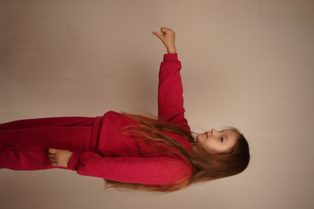 A girl with vibrant red hair demonstrates a "dislike" gesture using one hand. Her intent look conveys disapproval. The light, neutral background complements her striking presence.の写真素材