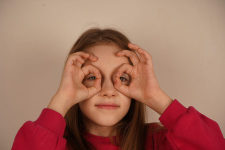 A charming moment of youthful imagination. A little girl playfully forms her fingers into an OK...