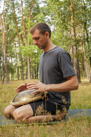 A boy in the middle of the forest plays a metal glucophone with his hands. A man in the middle of...