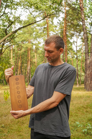 In the middle of a pine forest, a boy shows off a wooden board with drawings on it.の写真素材