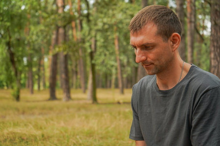 Close-up of a man in a dark T-shirt on a green forest background. Handsome man of European appearance. Summer atmosphere of the forest.の写真素材