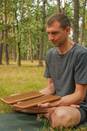 A peaceful scene of a man meditating in nature, surrounded by tall trees. Wooden sadhu boards on the mat enhance the meditative vibe.の写真素材
