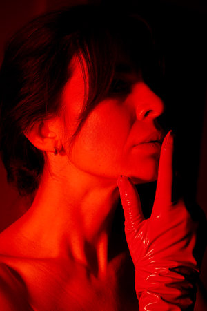 Close-up of a womans face with gloved fingers elegantly posed near her lips, set against a dark background with contrasting dramatic lighting, creating a striking and mysterious visual.の写真素材