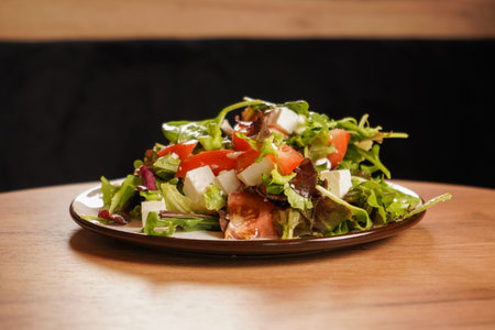 Healthy vegetable salad with tomatoes, feta cheese and herbs on a plate. The salad is on a wooden...