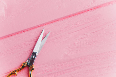 Close-up of gold-tipped iron scissors on pink boards. Scissors for needlework on the table.の写真素材