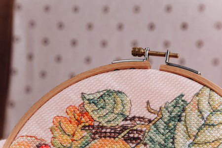 An embroidery hoop with a bright floral pattern is shot close-up against a pale pink background. Do-it-yourself aesthetic installation.の写真素材